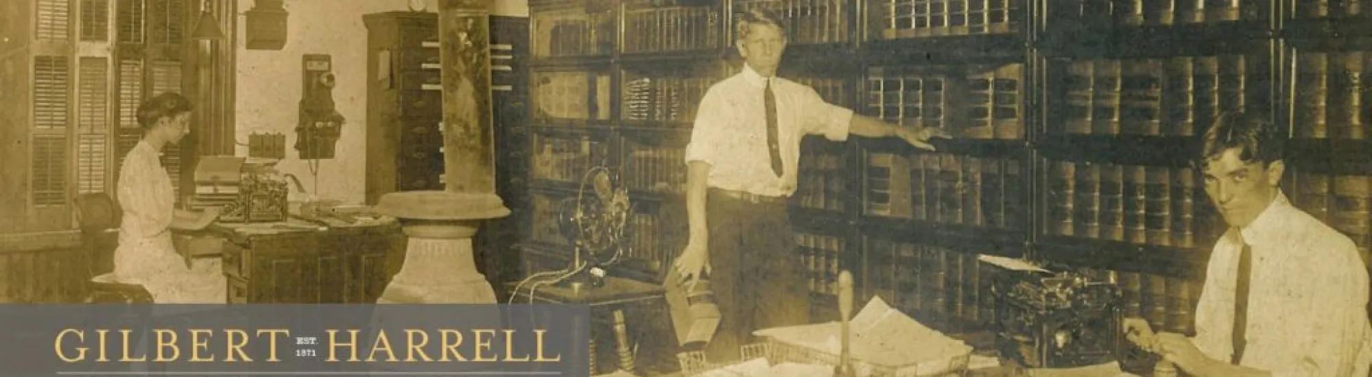 Sepia-toned photo of a vintage office with three men, shelves of books.